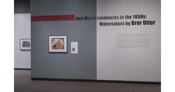 Exhibition title wall; the left half is dark gray and features a framed watercolor of a church; the right half is light gray and features exhibition text.