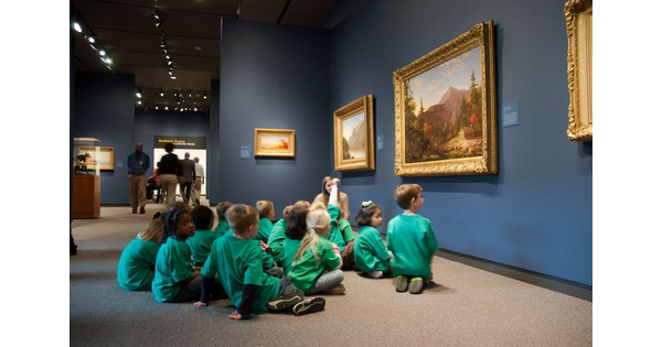 School children sit on the floor of a Carter gallery in front of several paintings.