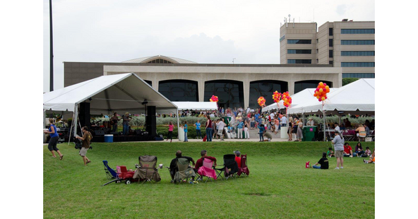 People sit in lawn chairs in the grass in front of the Carter watching entertainment under tents.