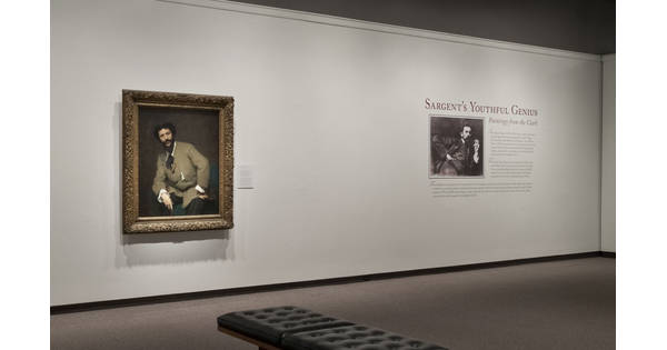 Exhibition title wall showing a framed portrait, the exhibition text and a photo of the artist.