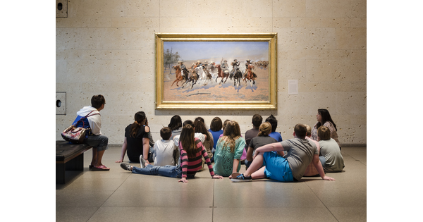 A group of middle-school students at the Carter sit on the floor in front of a painting.