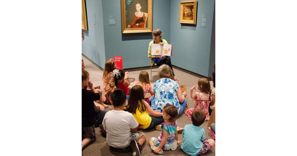 A Carter educator sits in front of an artwork and reads a story to a group of children sitting on the floor.