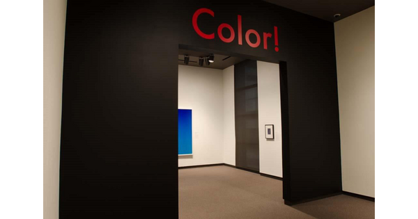 Entrance to an exhibition; a black wall with the word &quot;Color!&quot; in red above the entrance; part of an artwork can be seen through the entrance.