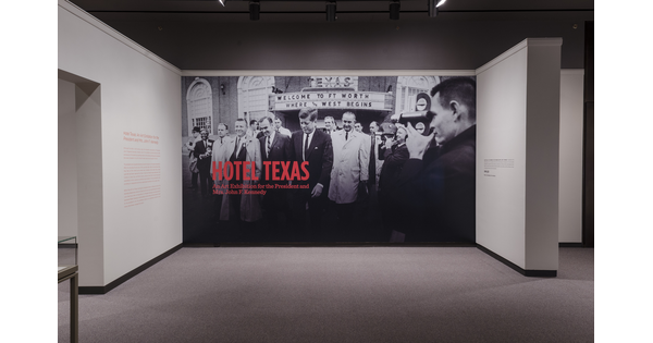 Exhibition title wall showing large-scale black-and-white photo of President Kennedy, surrounded by many people, visiting Fort Worth.