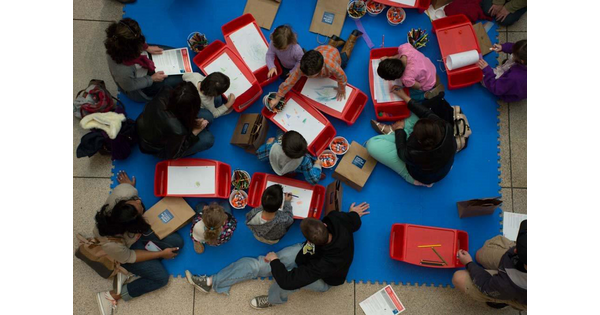 View from above of children and adults sitting on a floor creating art.