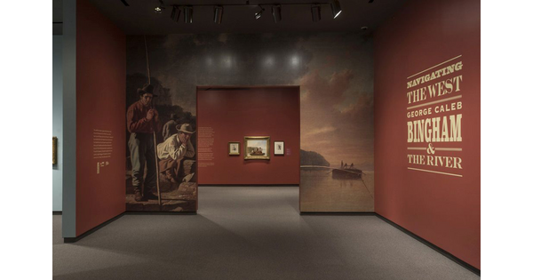 Entrance to exhibition showing the title wall on the right; the entrance is surrounded by and enlargement of a painting of men fishing; through the entrance are three framed artworks.