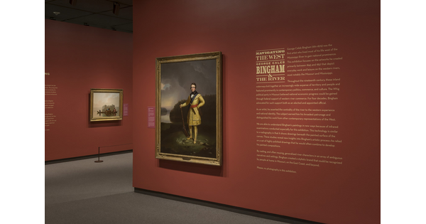 A dark orange-red wall featuring introductory text to the right of a gold-framed painting of a man standing on a hillside.