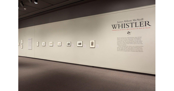 View of gallery showing exhibition title and introductory text and a row of framed prints to the left hanging on a white wall.