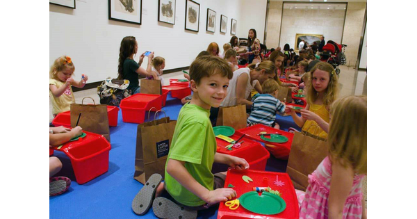 A large group of children and parents sit on a gallery floor at the Carter making art. 