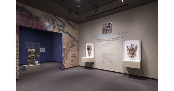 Exhibition entrance; on the right is the title wall and introductory text with two display cases containing native American objects; the entrance wall features a map of North America; through the entrance is a display case containing an object.