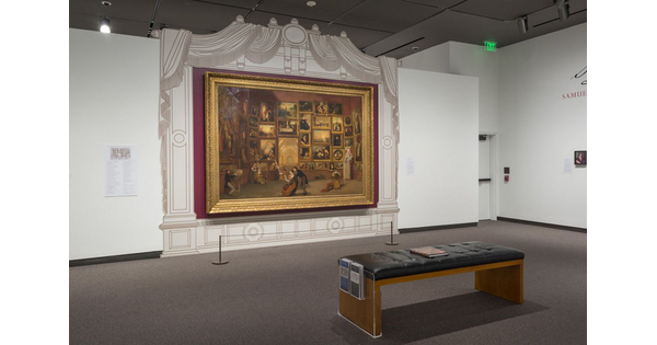 View of painting in a gold frame, surrounded by a fake proscenium; a bench for seating is in front of the painting.