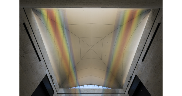 View of the ceiling of the museum&#039;s atrium showing the installation of two sections of colored thread stretched from wall to wall creating two rainbows.