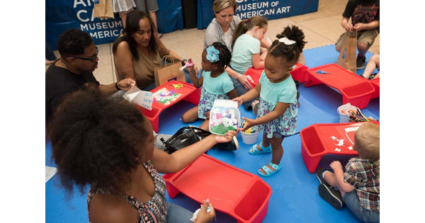 Adults and children sit on the floor in the Museum and work on art projects.