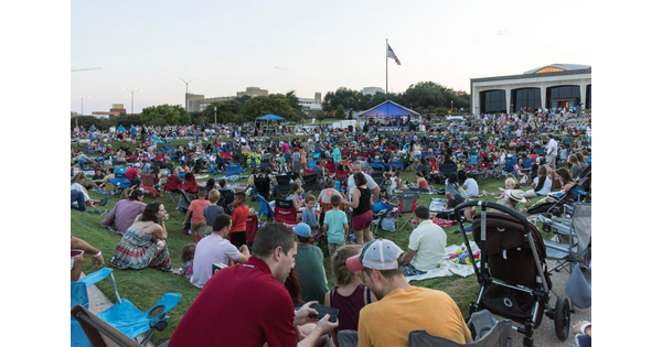 A large crowd of people sit and mingle on the grassy lawn in front of the Carter.