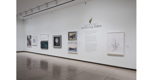 View of gallery with white walls; eight framed artworks hang on the wall around the exhibition title and introductory text.