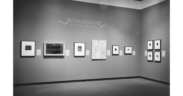 Black-and-white photo of gallery featuring framed photographs and a painting.