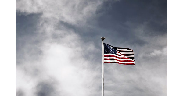 An American flag flies on a flagpole against white clouds and blue sky.