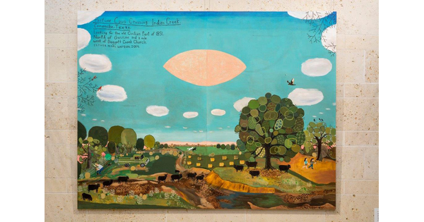 Large-scale painting hanging on a smooth stone wall; the top half shows blue sky, white clouds, and a football-shaped pink UFO; the bottom half shows rolling green hills and pastures, trees, and a herd of black cows.