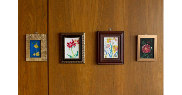 Four small framed paintings of flowers hang in a row on a wood wall.