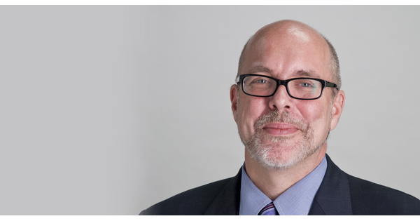 Headshot of a White man, bald with a goatee and black-framed glasses.