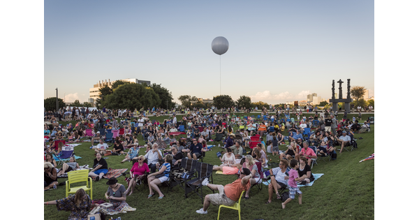 A large crowd of people sit and mingle on the grassy lawn in front of the Carter.