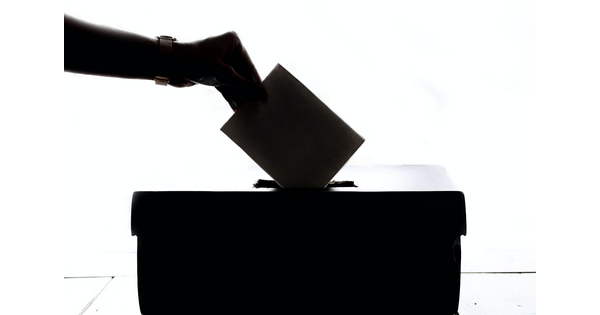 Image showing a silhouette of a hand placing a ballot into a box.