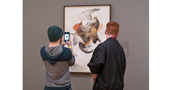 Two people, one taking a photo with a smartphone, stand in front of an artwork.