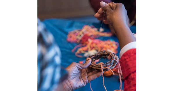 Close-up of a senior&#039;s hands using yarn and sticks to make an artwork.