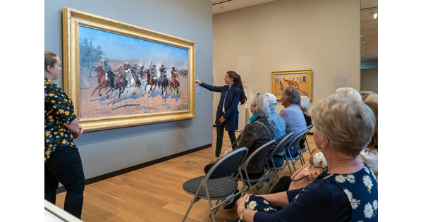 Senior adults sit as an educator gestures to artwork on the wall.