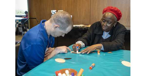 One adult helps another adult with an art project.