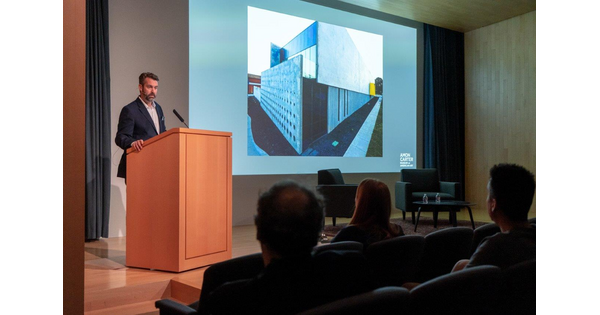 In the Carter&#039;s auditorium, a man stands at a podium next to a screen showing artwork.