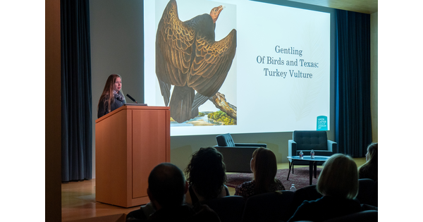 In the Carter&#039;s auditorium, a woman stands at a podium next to a screen showing artwork.