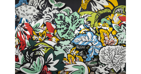 A detail of an installation of large wood cut-outs of flowers and leaves, some brightly-colored, against a black wall with shadows projected on the floor in a Carter gallery. 