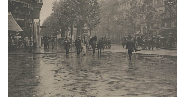 A black-and-white photograph of people crossing a city street in the rain.