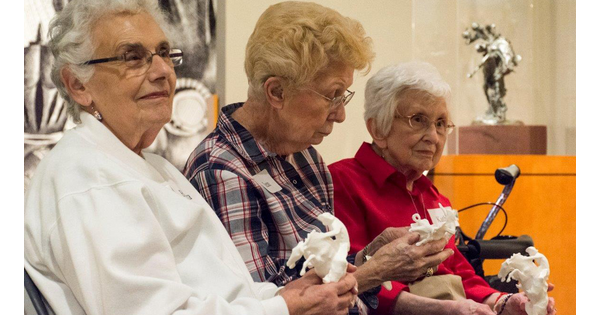 Three seniors sit in a Carter gallery holding replicas of a sculpture.