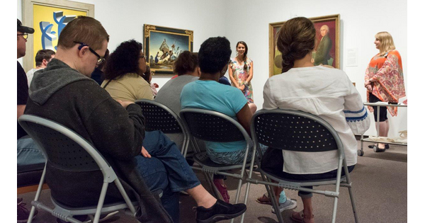 A group of adults sit in a Carter gallery listening to a tour.