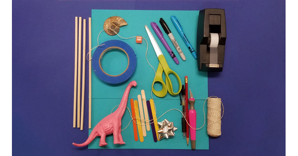 Art supplies and a pink brontosaurus laid out on a table.
