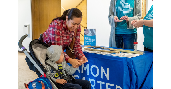 An adult shows an art activity to a young child in a stroller as Carter educators watch.