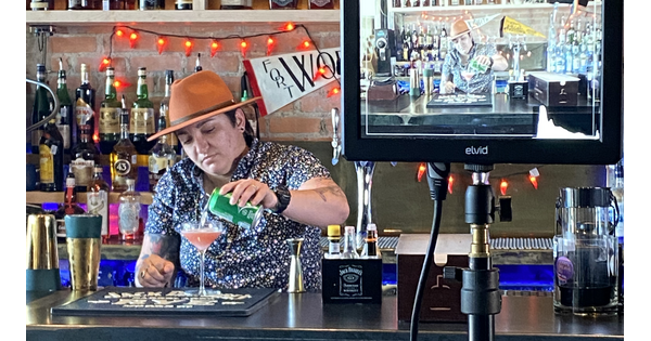 A person stands behind a bar pouring a soda into a martini glass.