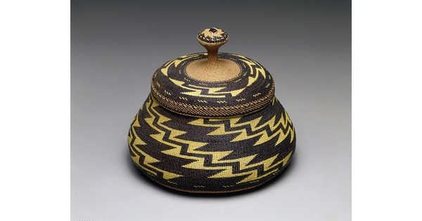 A woven basket and lid with a yellow and black zig-zag pattern.