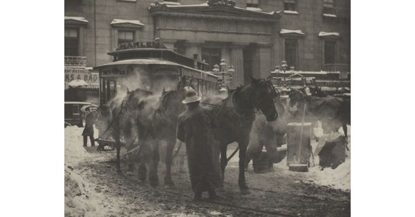 A black-and-white photograph of horses pulling a trolley on a busy street covered with slush and snow.