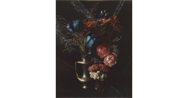 A color photograph of a variety of blue, purple, red, and pink flowers in a gold amphora-style vase.