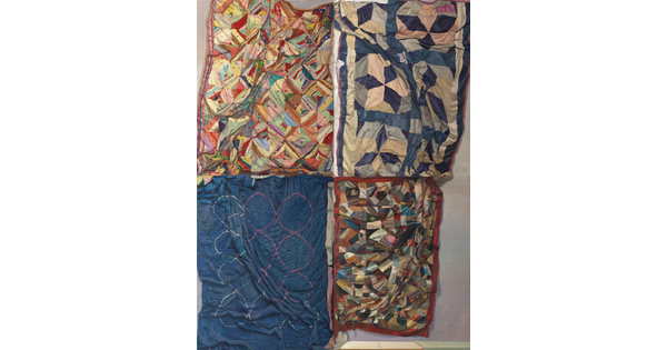 A realistic oil painting of four rumpled quilts.