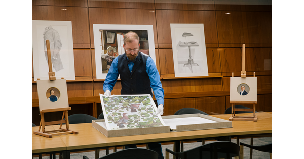 Archivist Jon Frembling gently lifts a print out of a box with his gloved hands.