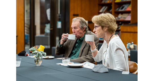 Two people sit at a table and sip on tea.