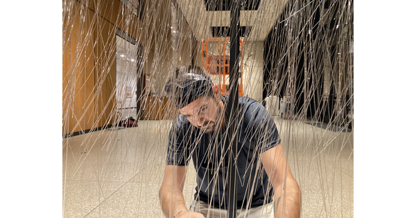A White man kneels on the floor of a Carter gallery arranging threads of glass.