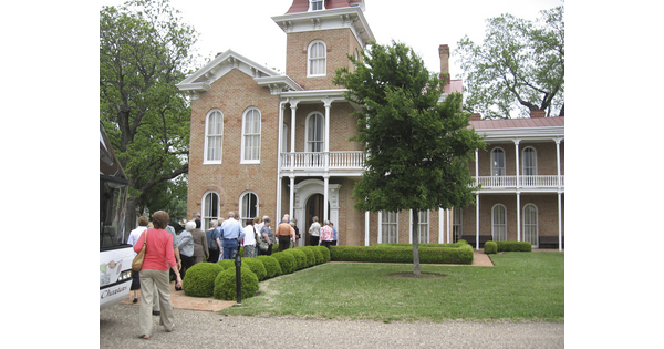 A group of people file into a two-storey brick mansion.