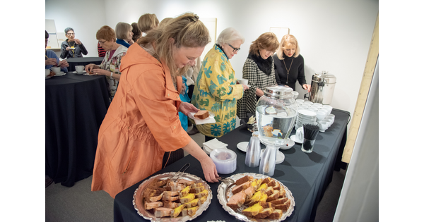 Adults stand in front of a table serving themselves tea and pastries.