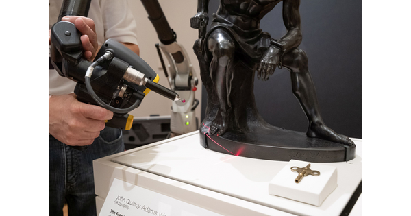 A red light from a laser gun moves over the surface of a bronze sculpture.