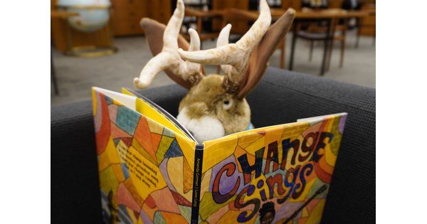 A jackalope sits in a comfy chair in the Carter Library reading a book.